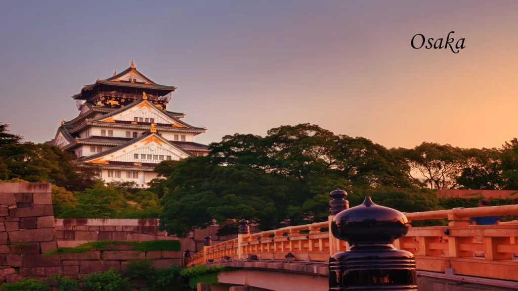 The majestic Osaka Castle tier rising above lush green trees and a traditional wooden bridge at sunset during a 7 days tour in Japan.