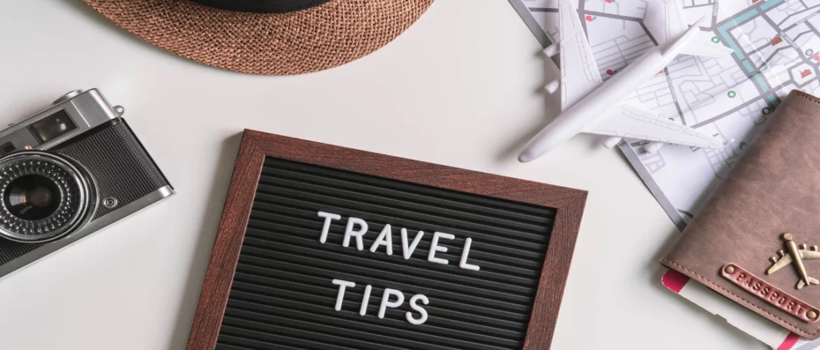 Flat lay of a camera, straw hat, passport, map, toy plane, and travel tips letterboard for trip planning inspiration.