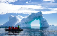 Antarctica tourism 2026 Antarctica glacier arch with tourists exploring by boat