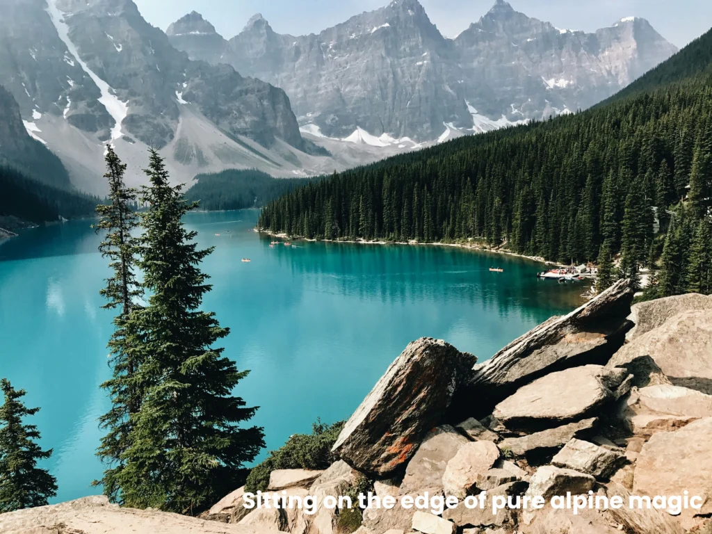 Panoramic viewpoint over Moraine Lake's bright turquoise waters framed by rocky boulders and pine trees.